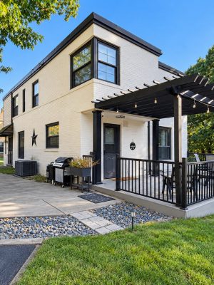 A white brick home with a covered pergola deck just outside the front door.